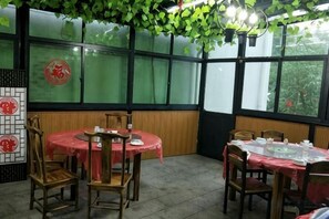 A restaurant with round tables and chairs, a green wall with a red emblem, and large windows. - Anjiyingjun (Anji)