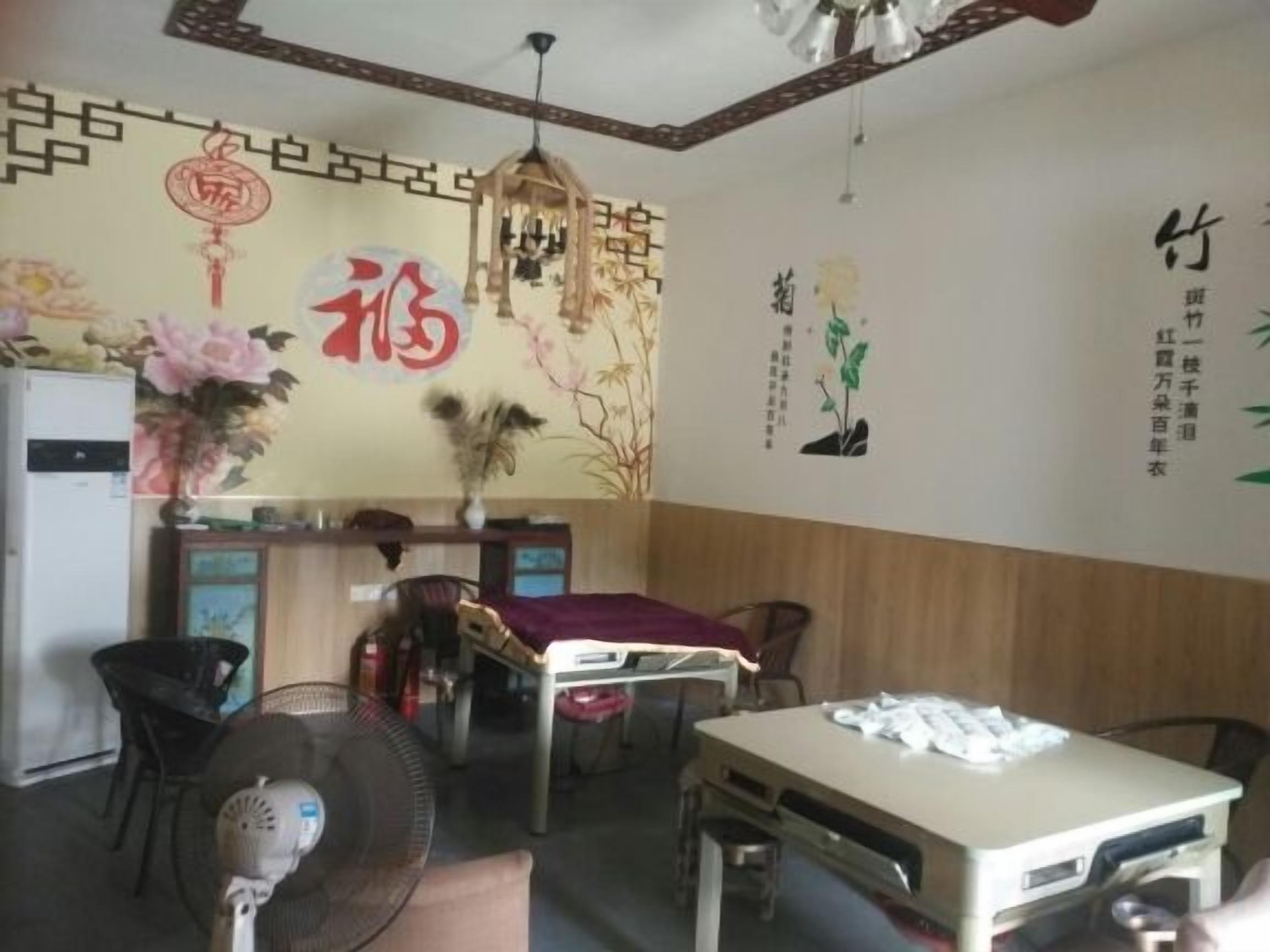 A room with a bed, a desk, a chair, a fan, and a wall with decorative elements.
