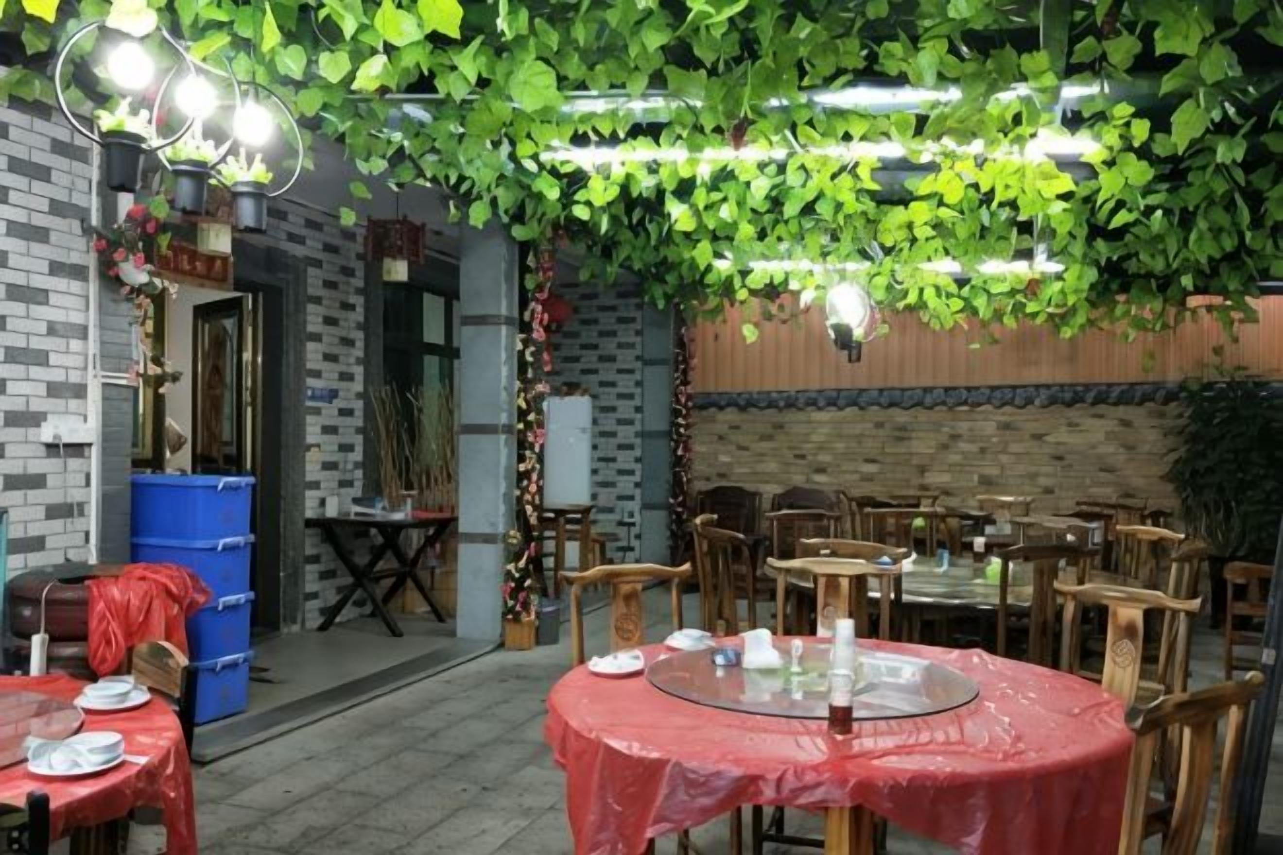 An indoor dining area with tables covered in red tablecloths, wooden chairs, and hanging greenery.