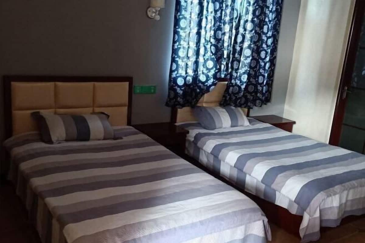 A room with two beds, a window with patterned curtains, and a wall-mounted light fixture.