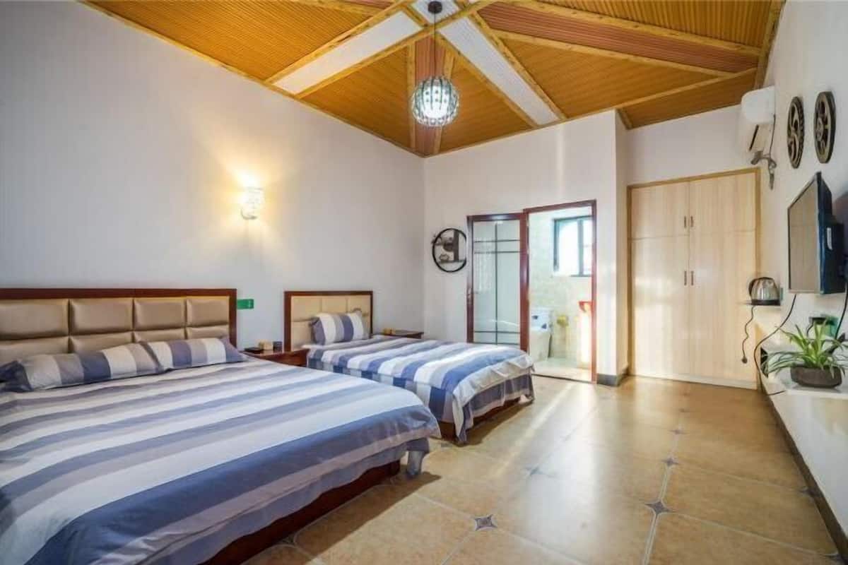 A bedroom with two beds, a wooden ceiling, a chandelier, a wardrobe, and a door leading to another room.