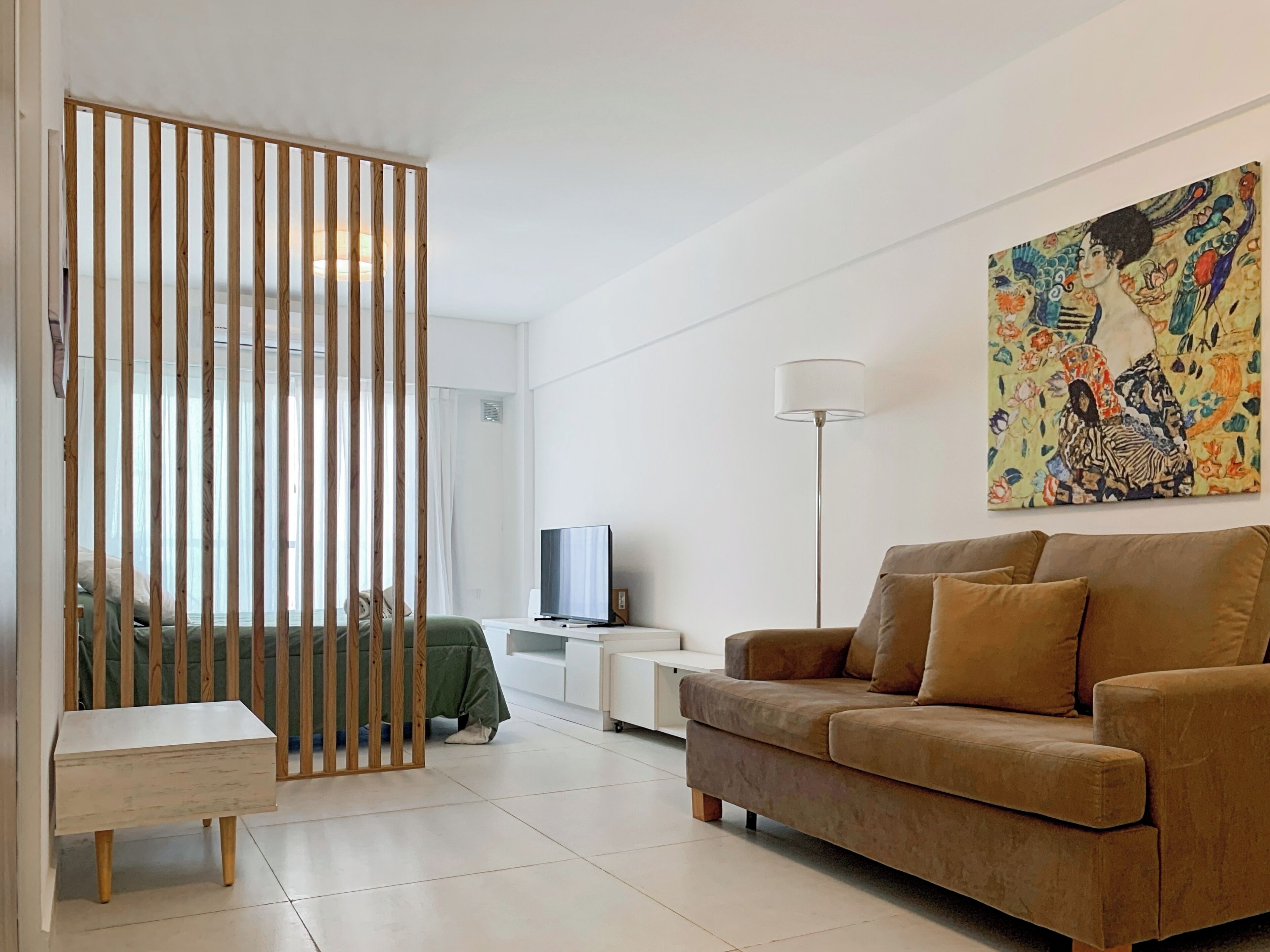 A modern living room with a sofa, a TV, a floor lamp, and a painting on the wall.