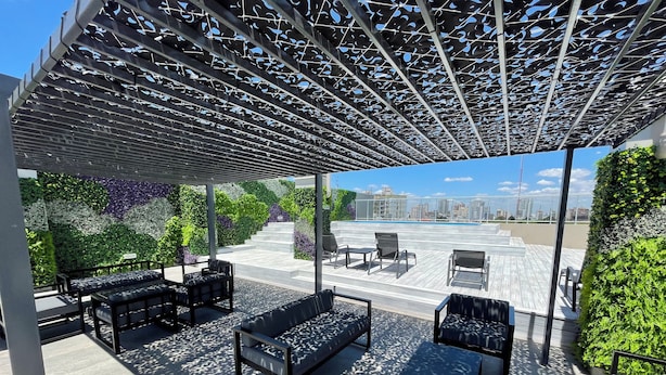 Eine Dachterrasse mit Sitzgelegenheiten im Freien, einer Pergola und Blick auf die Stadt.