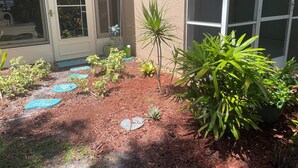 A landscaped garden with various plants and stepping stones leading to a door. - 1st Floor Charming 2-bedroom condo in Bonita Springs with Community Pool (Bonita Springs)