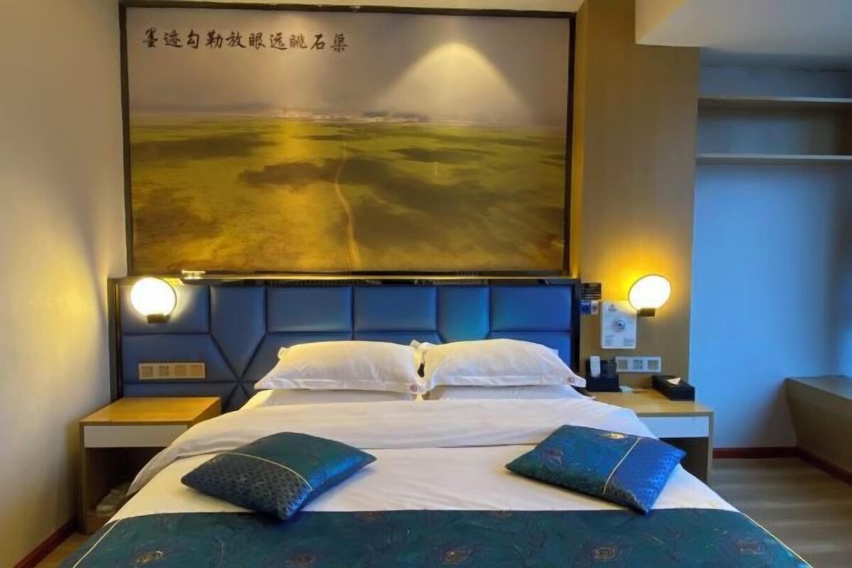 A hotel room with a large bed, two bedside lamps, a headboard, and a wall-mounted artwork.