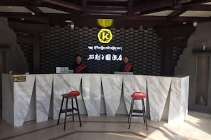 Un mostrador de recepción con encimera de mármol y dos taburetes rojos acolchados. Detrás del mostrador, una pared con estampado blanco y negro presenta un logotipo y texto.