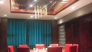 A dining area with a round table, red upholstered chairs, teal curtains, and a modern ceiling design. - Shike Wangguo Hotel (Shiqu)