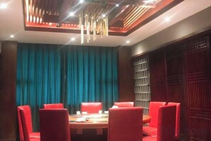 A dining area with a round table and red chairs, a teal curtain backdrop, and a modern ceiling design. - Shike Wangguo Hotel (Shiqu)