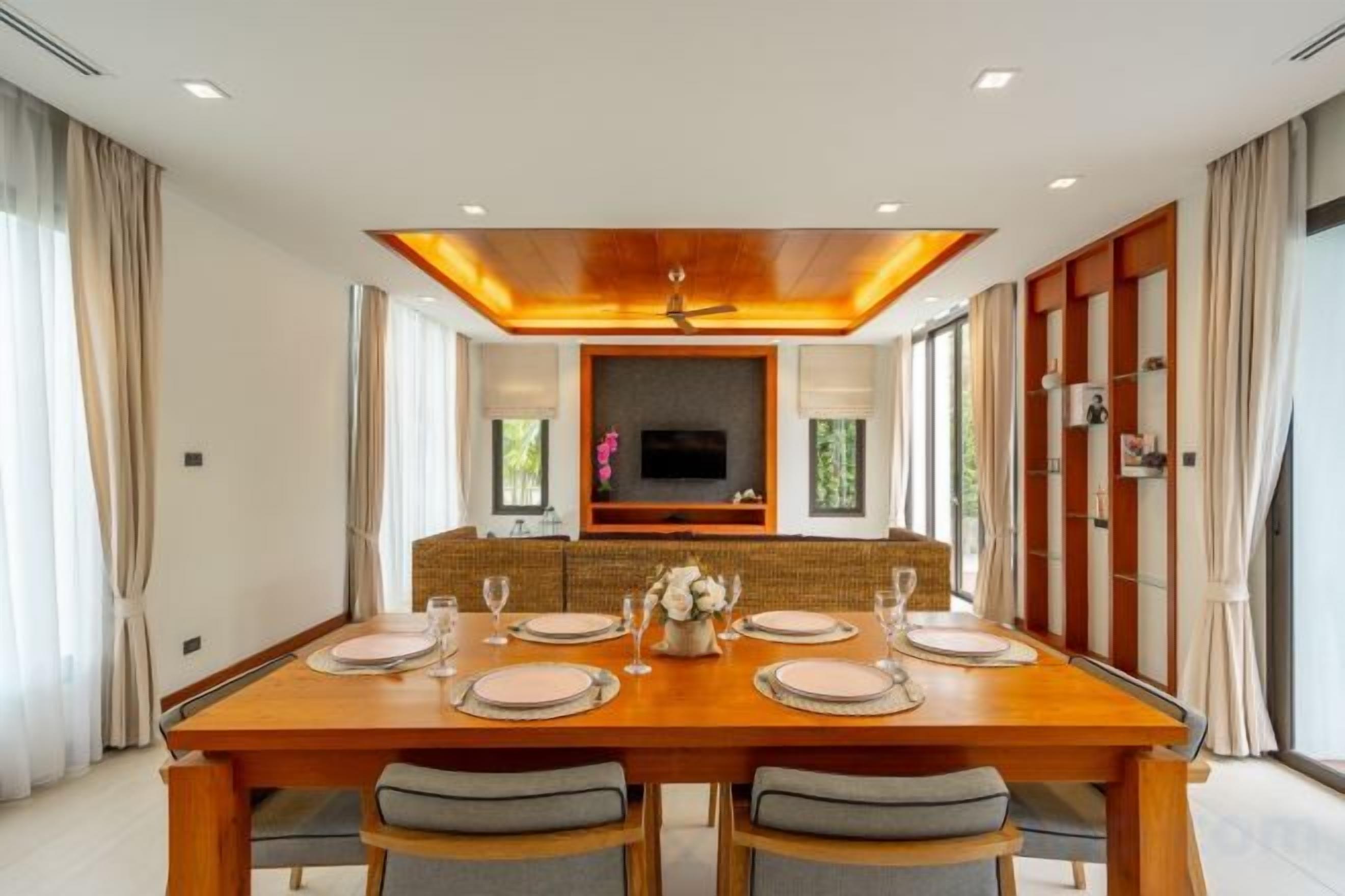 Un comedor con una larga mesa de madera, seis sillas y una pantalla de televisión encima.
