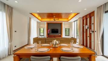 Un comedor con una larga mesa de madera, seis sillas y una pantalla de televisión encima.