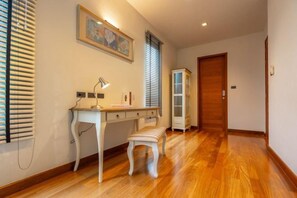 Un pasillo con suelo de madera, un escritorio con lámpara, un banco y una puerta.