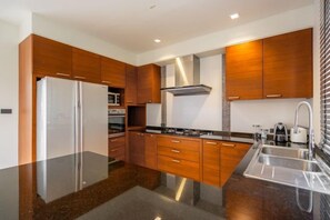 A modern kitchen with wooden cabinets, stainless steel appliances, and a black countertop. - Villa Autjima Krabi /3Brd (Krabi)