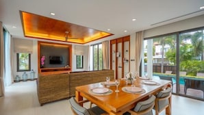 Un espace repas moderne avec une table en bois disposée pour quatre personnes, un téléviseur intégré et une grande fenêtre donnant sur l’extérieur.