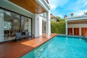 Un área moderna junto a la piscina con terraza de madera, sillas de descanso y una piscina azul cristalina.