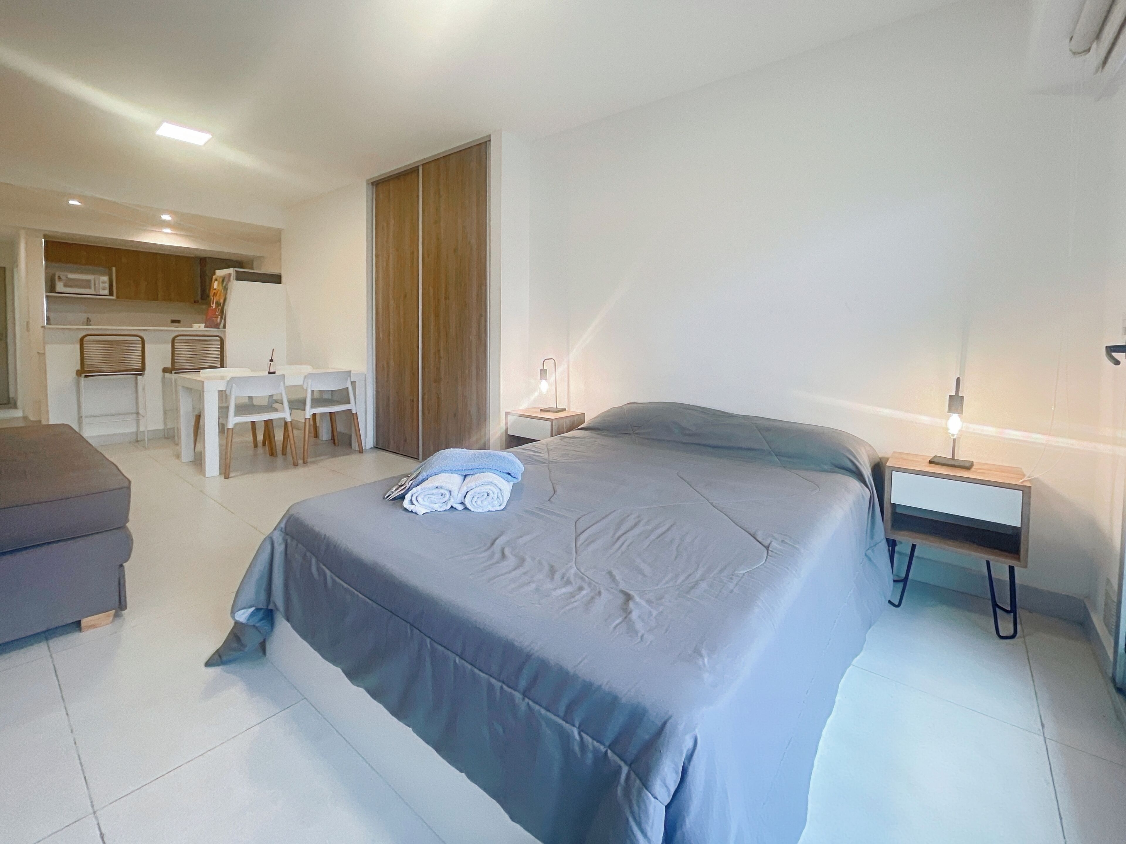 Ein modernes Hotelzimmer mit einem großen Bett, einem Nachttisch mit Lampe, einem kleinen Schreibtisch und einem Essbereich mit Stühlen und Tisch.