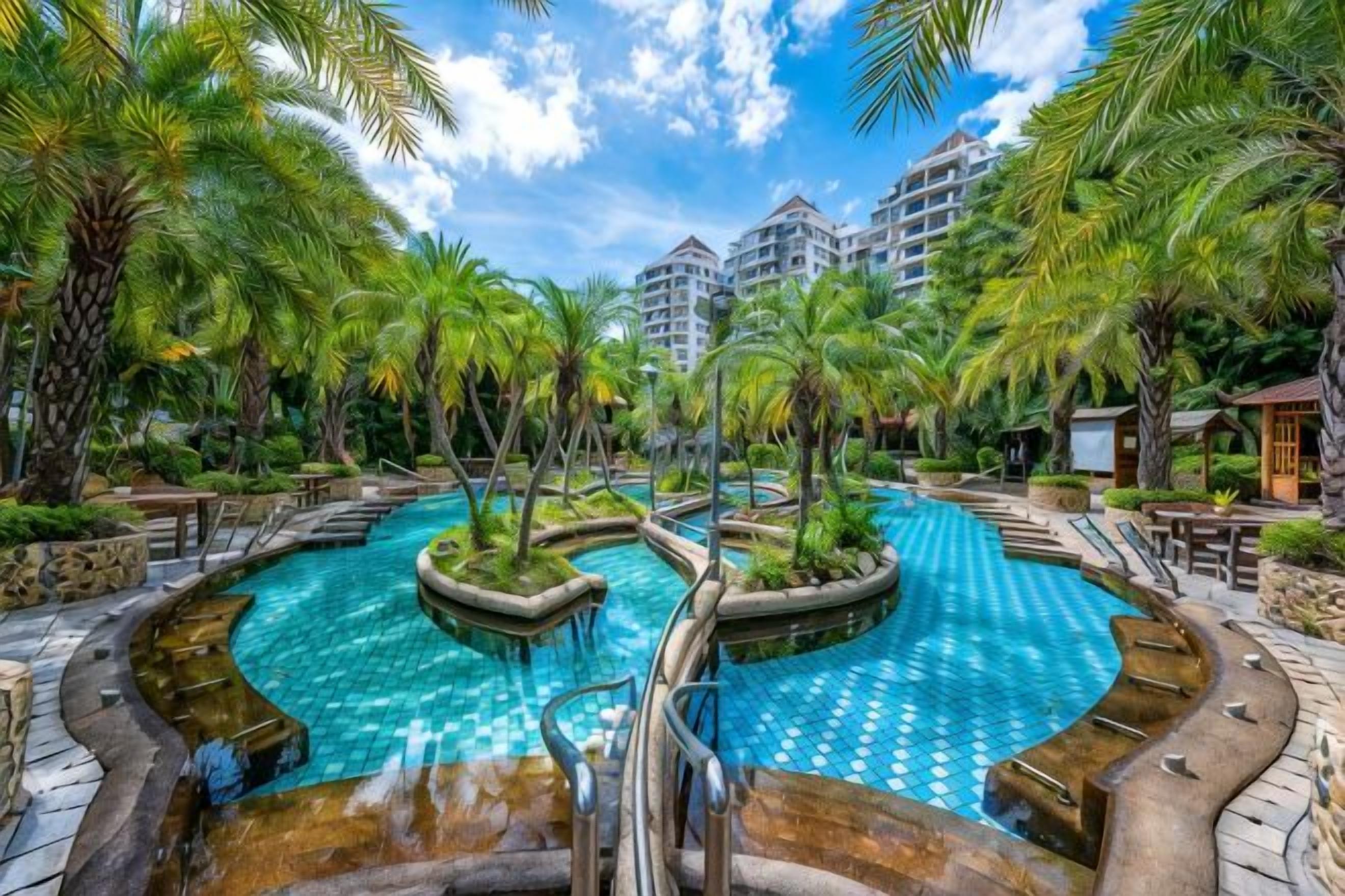A swimming pool surrounded by palm trees and a hotel building in the background.