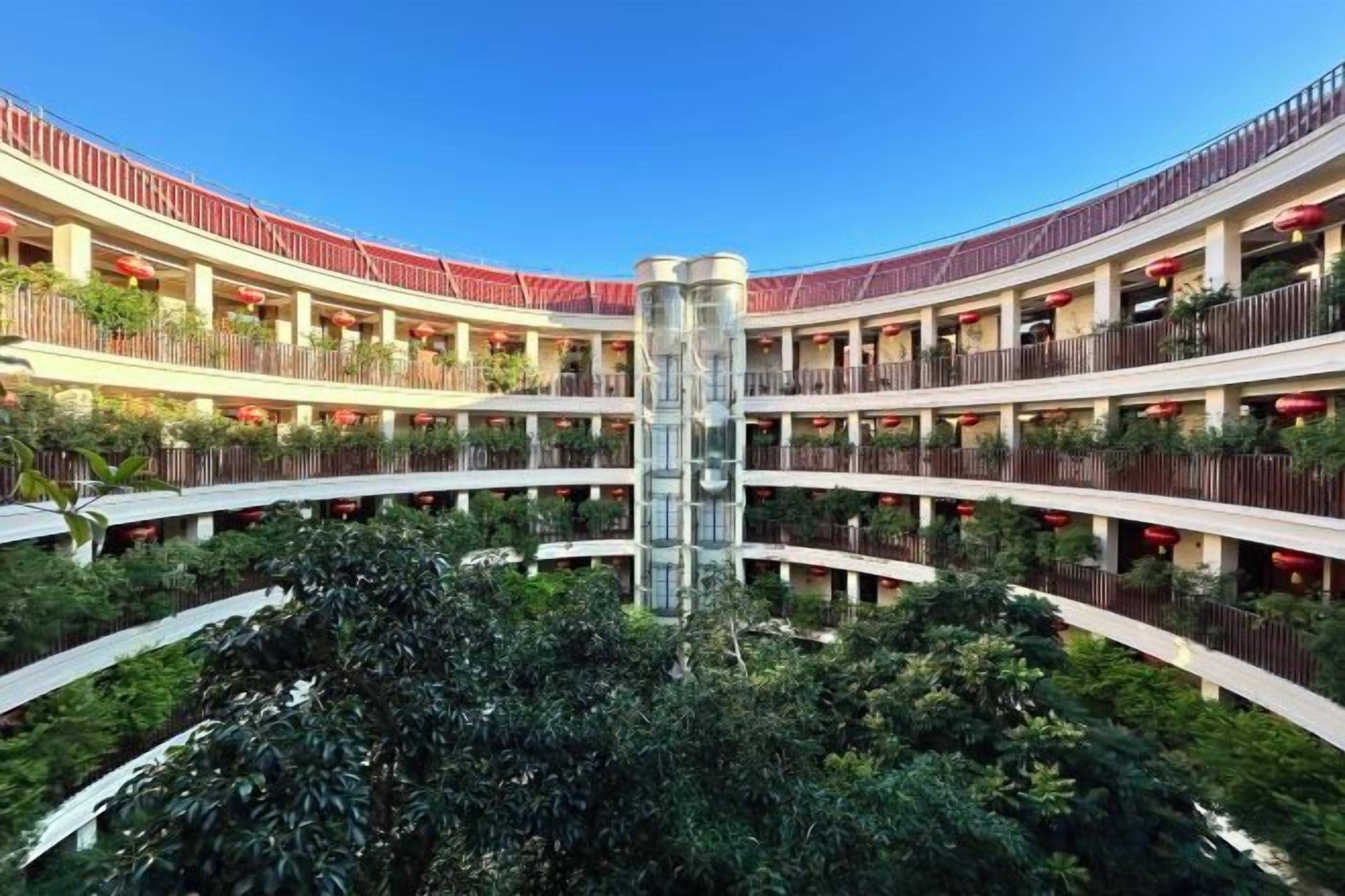 A multi-level hotel atrium with a central glass column, surrounded by balconies and greenery.
