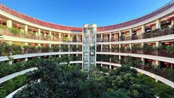 A multi-level hotel atrium with a central glass column, surrounded by balconies and greenery.