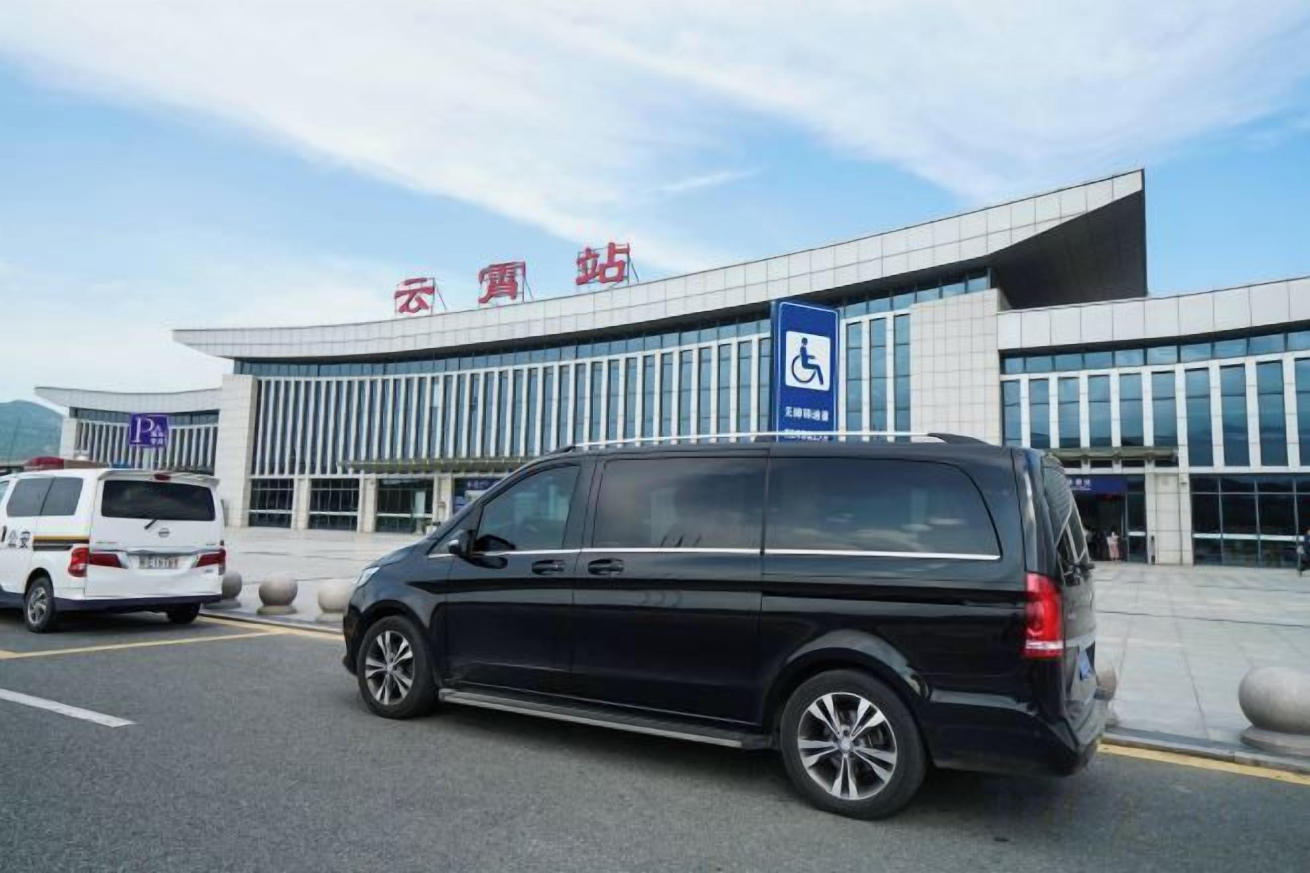 A modern building with a blue handicap parking sign, a black car, and a white van parked in front.