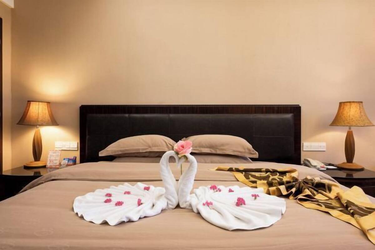A hotel room with a neatly made bed, two bedside lamps, and a bouquet of flowers on the bed.