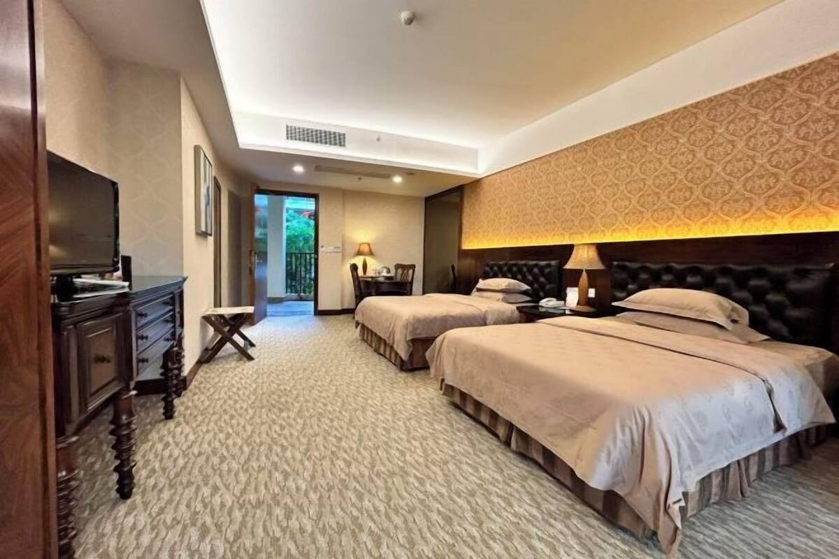 A hotel room with two beds, a desk, a TV, and a patterned wall.