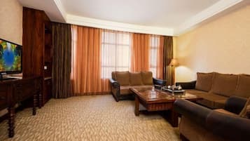 Una habitación de hotel con un ventanal grande, un sofá, una mesa de centro, un televisor y una lámpara.