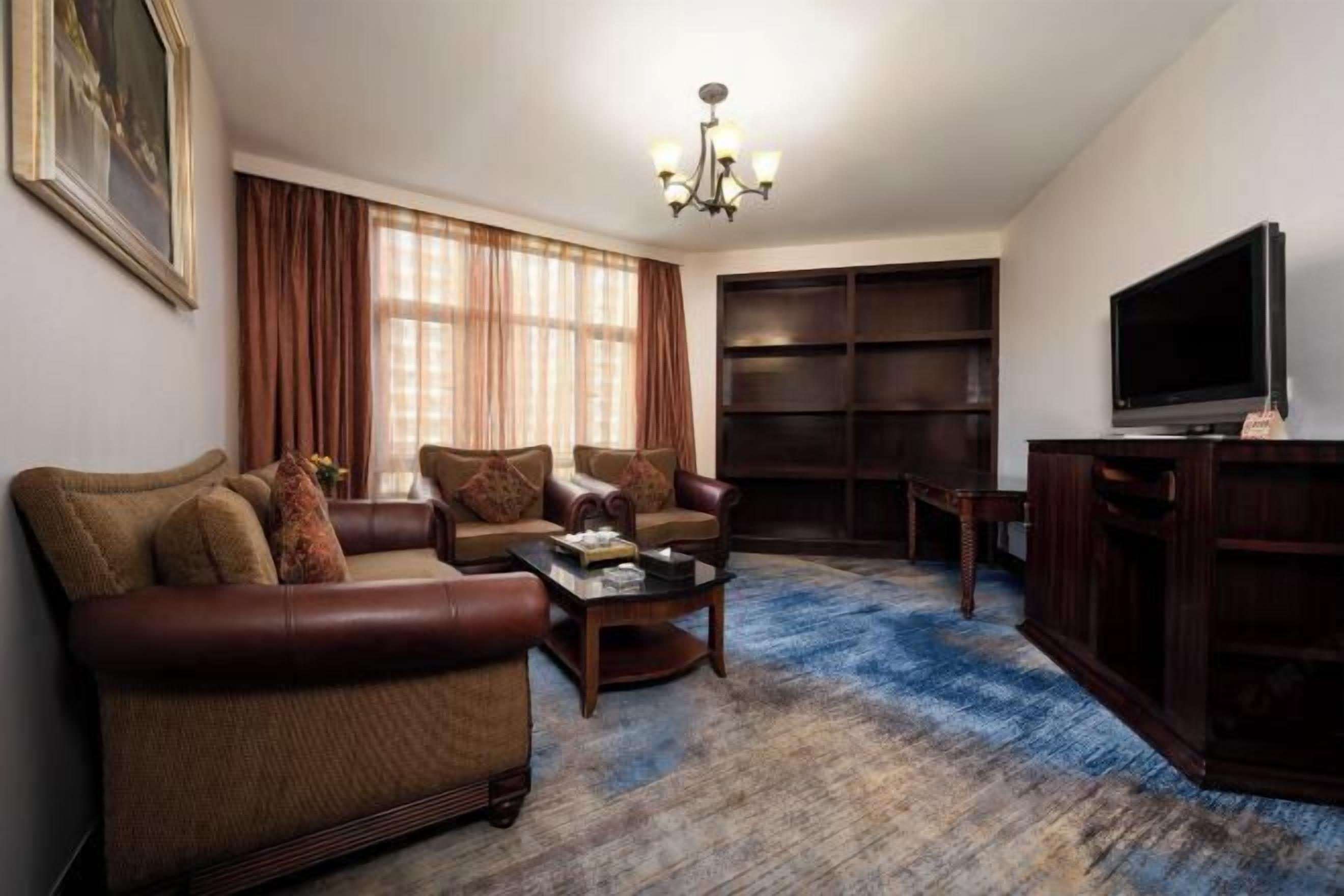 A living room with a sofa, armchairs, a coffee table, a TV, and a bookshelf.