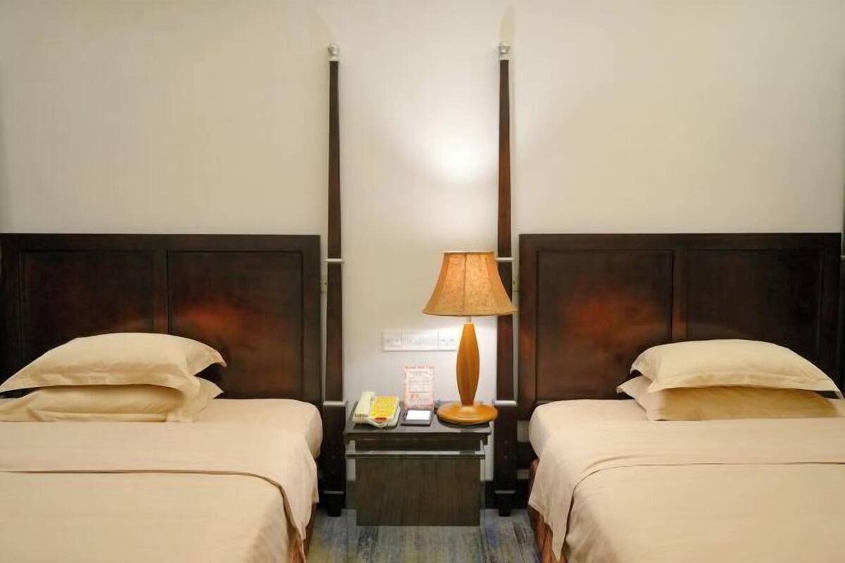 A hotel room with two beds, a nightstand with a lamp, a phone, and a small table.