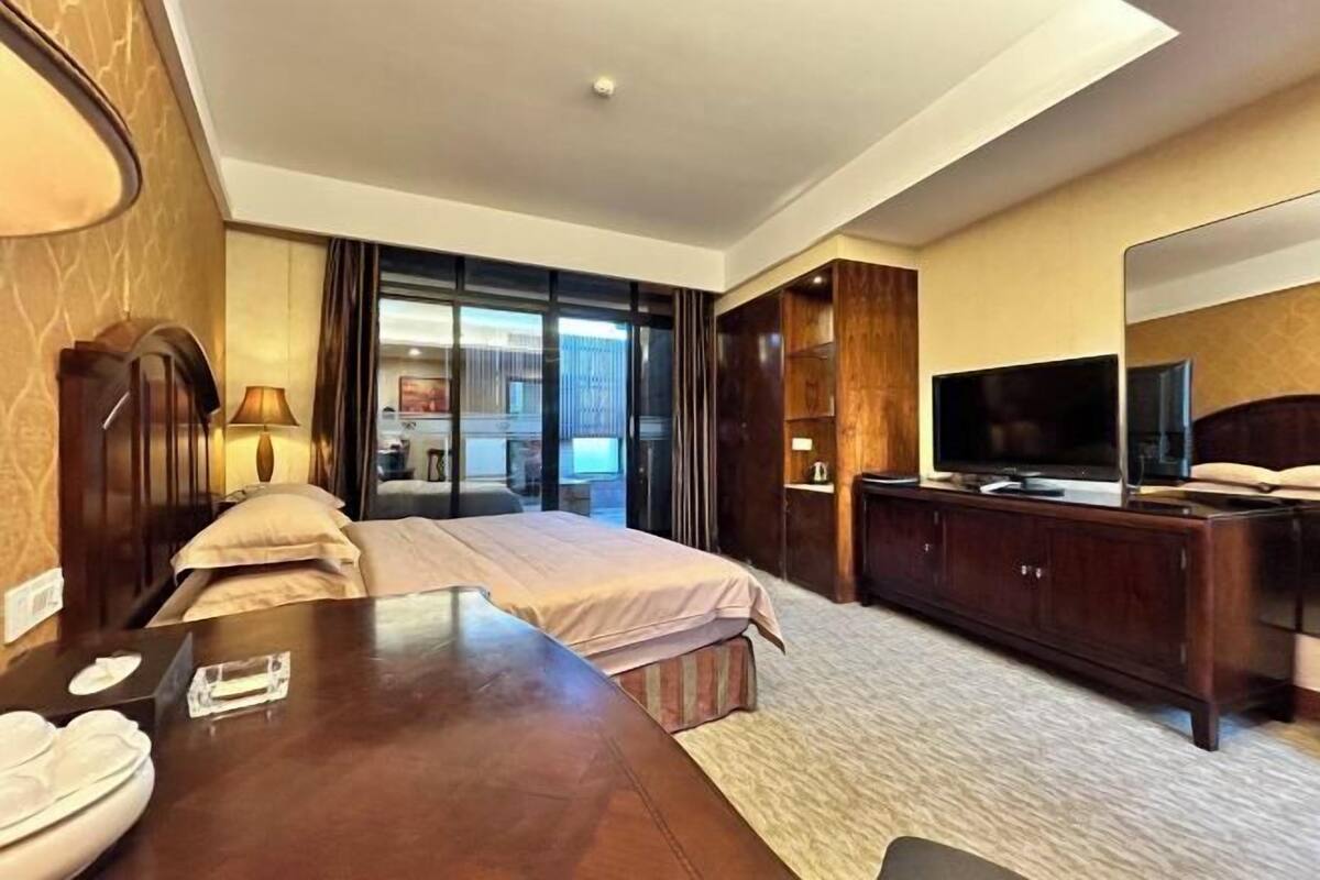 A hotel room with a bed, a desk with a telephone, a television, and a large window.