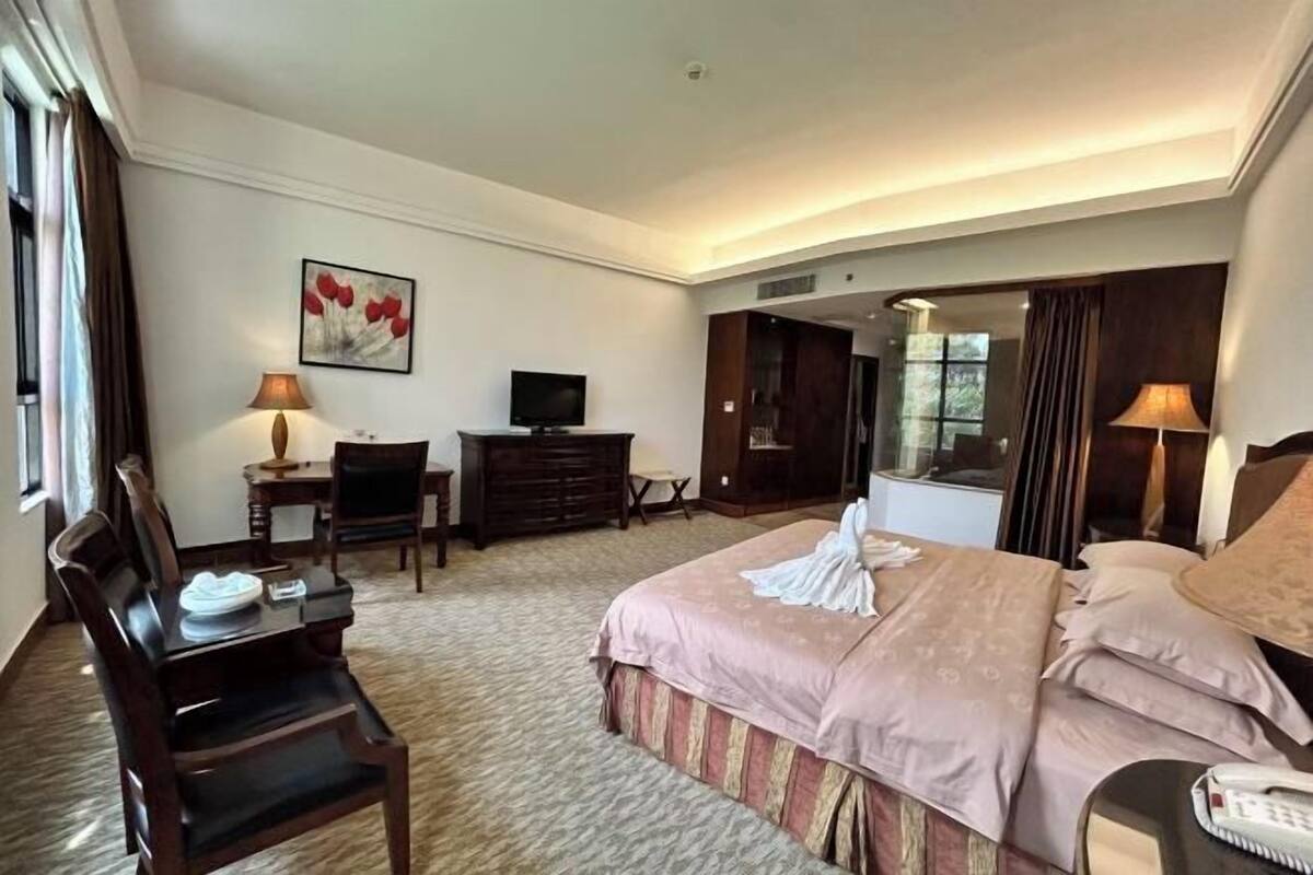 A hotel room with a large bed, a desk with a chair, a television, and a mirror.