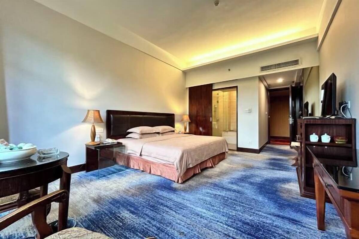A hotel room with a bed, bedside table, lamp, and a television.