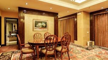A dining area with a round table and six chairs, a chandelier, a framed floral painting, and a patterned carpet.