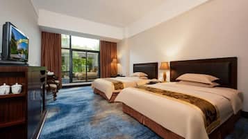 Habitación de hotel con dos camas, televisión, escritorio y vistas a zonas verdes.