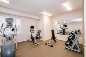Ett gym med konditionsmaskiner, utrustning för styrketräning och en stor spegel.