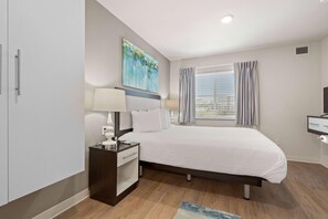 A modern bedroom with a bed, bedside tables, a nightstand, a painting, and a window with curtains. - Waterwalk Extended Stay Kansas City - Overland Pk (Overland Park)