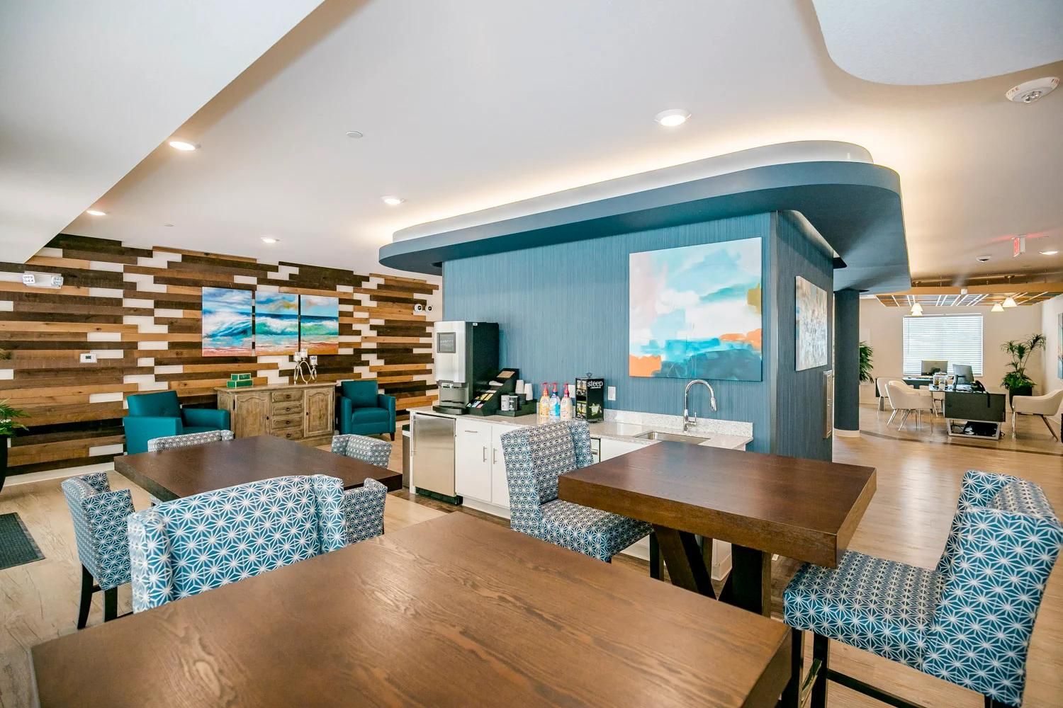 Een moderne hotelkamer met een houten wand, een kitchenette en een zithoek met gestreepte stoelen.