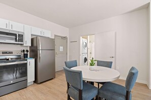 Een moderne keuken met roestvrijstalen apparatuur, een eethoek met blauwe stoelen, en een zichtbare wasruimte.