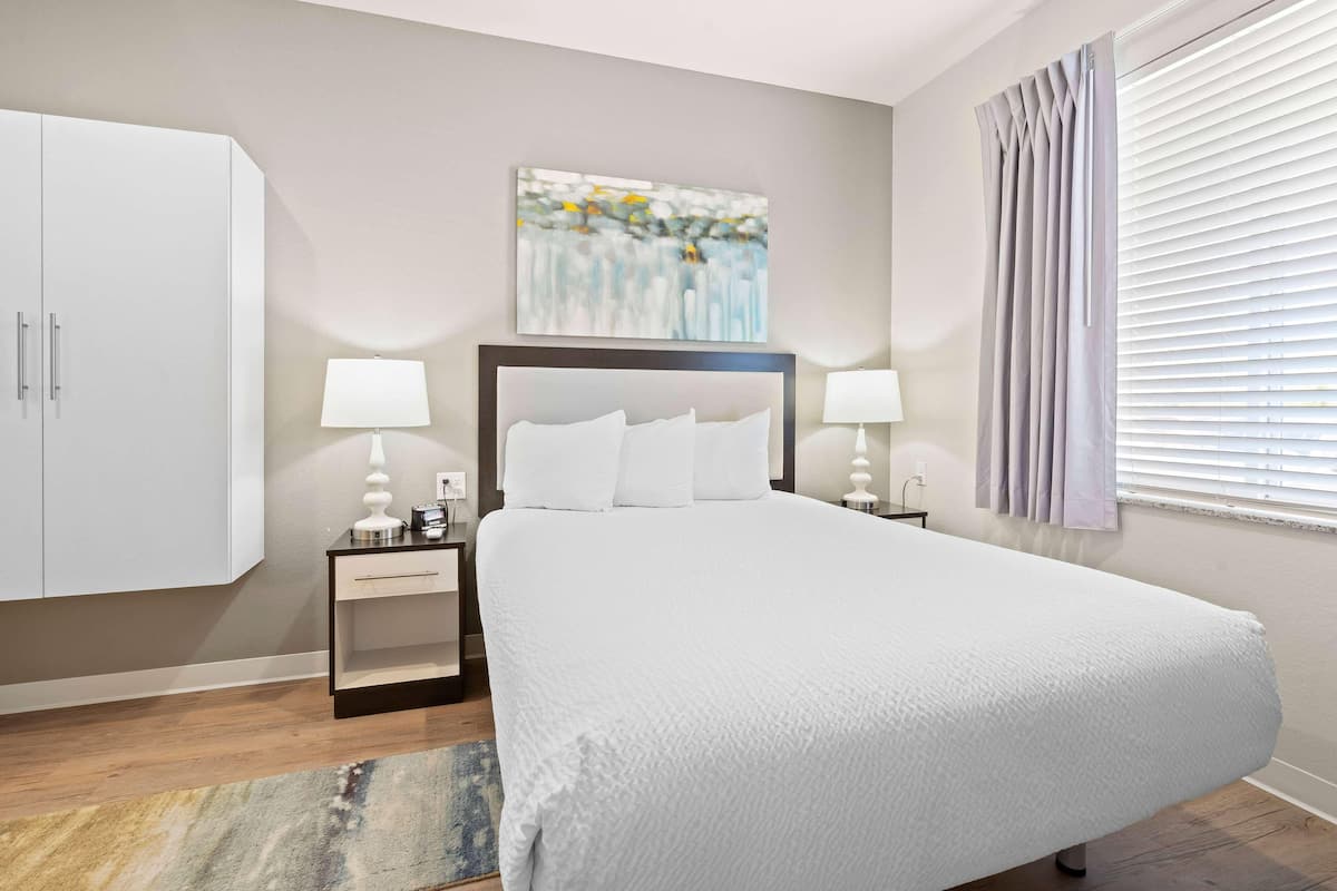 A neatly arranged bedroom with a large bed, bedside tables with lamps, a wardrobe, and a painting on the wall.