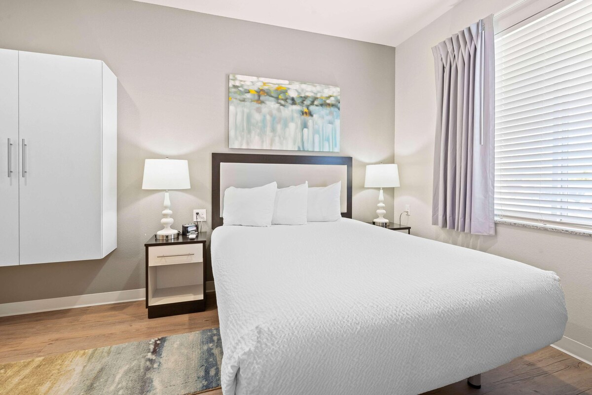 A neatly arranged bedroom with a large bed, bedside tables with lamps, a wardrobe, and a painting on the wall.