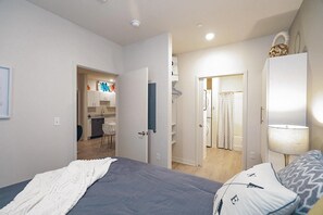 A bedroom with a bed, a bedside table, a lamp, and a wardrobe. There is a bathroom visible through an open door. - Waterwalk Extended Stay Kansas City - Overland Pk (Overland Park)