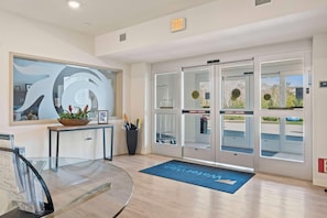 A modern reception area with a glass desk, a potted plant, and a blue mat with directional arrows. - Waterwalk Extended Stay Kansas City - Overland Pk (Overland Park)