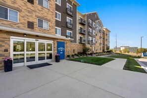 Un immeuble d’appartements à plusieurs étages, doté d’une façade en briques, d’une porte d’entrée bleue et d’une pelouse bien entretenue.