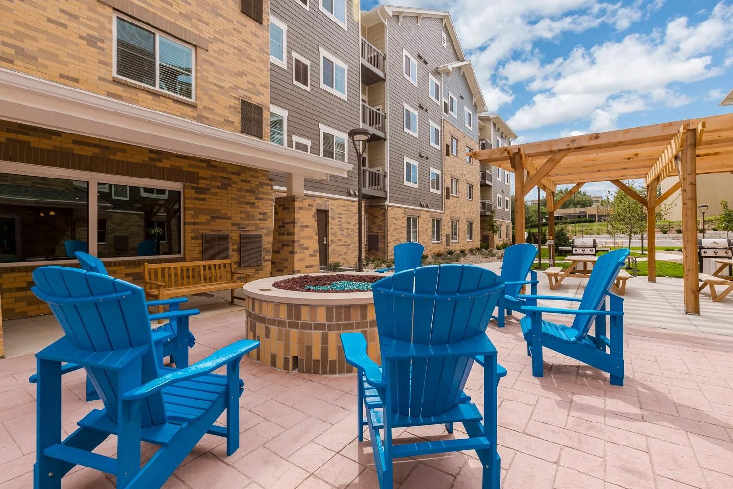 An outdoor patio area with blue Adirondack chairs, a fire pit, and a wooden pergola.