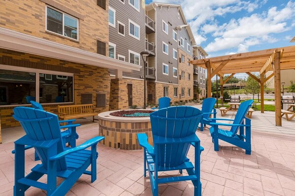 An outdoor patio area with blue Adirondack chairs, a fire pit, and a wooden pergola.