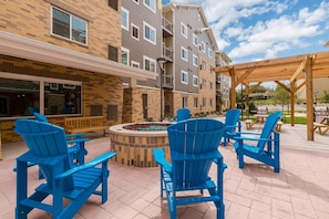 An outdoor patio area with blue Adirondack chairs, a fire pit, and a wooden pergola. - Waterwalk Extended Stay Kansas City - Overland Pk (Overland Park)