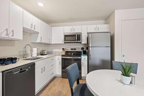 A modern kitchen with white cabinets, stainless steel appliances, a dishwasher, and a dining area with a table and chairs. - Waterwalk Extended Stay Kansas City - Overland Pk (Overland Park)