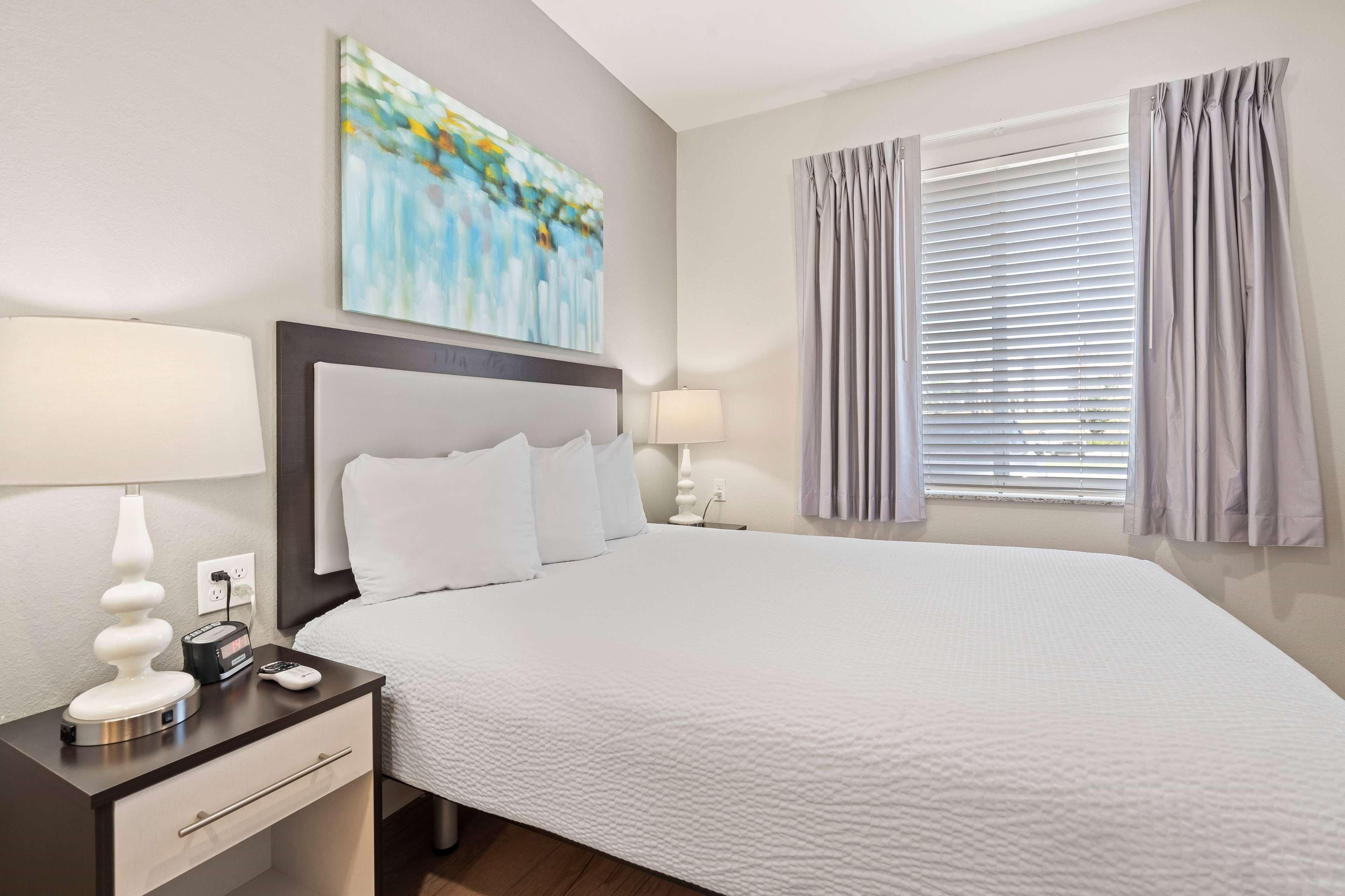 A neatly arranged hotel room with a large bed, bedside lamps, a nightstand, and a painting on the wall.