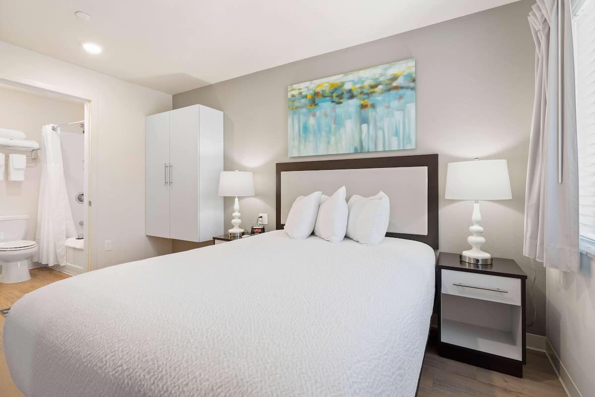 A hotel room with a large bed, two bedside tables with lamps, a wardrobe, and a painting on the wall.