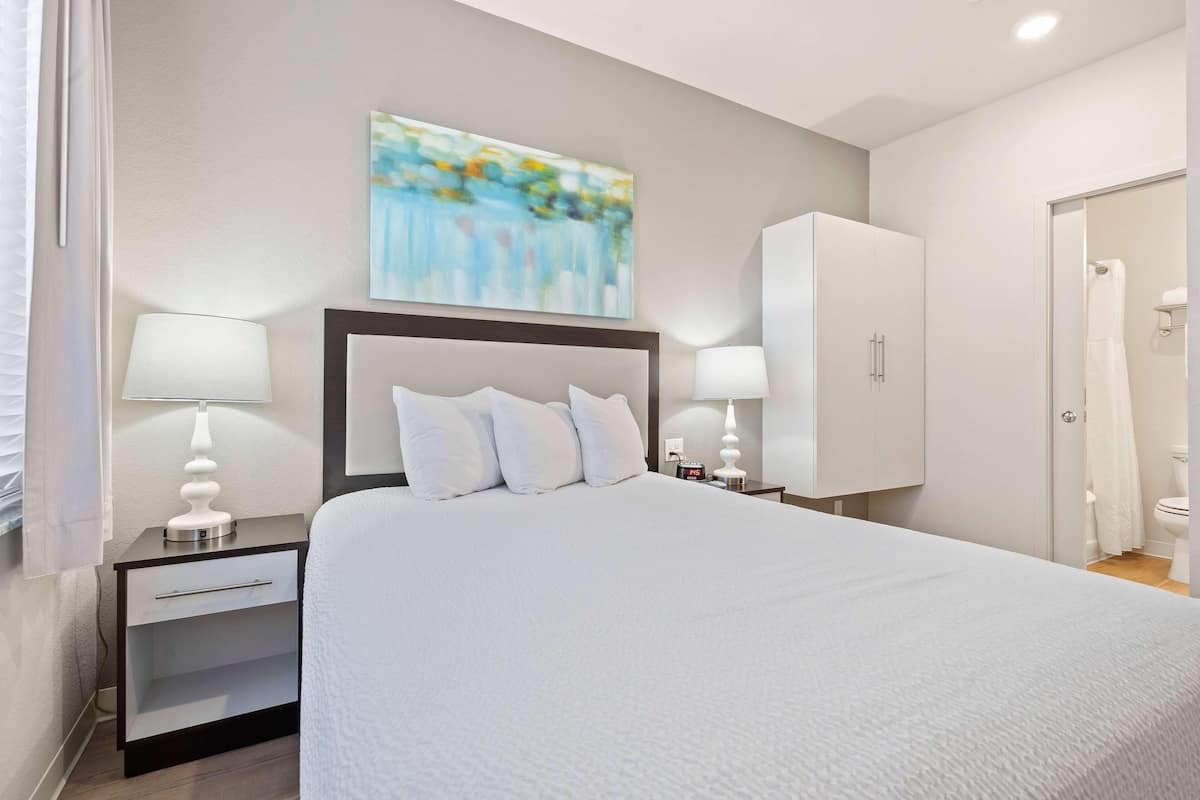 A neatly arranged hotel room with a large bed, bedside tables with lamps, a wardrobe, and a painting on the wall.