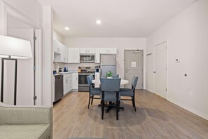A modern kitchen with white cabinets, a microwave, a refrigerator, and a dining area with a round table and four chairs. - Waterwalk Extended Stay Kansas City - Overland Pk (Overland Park)
